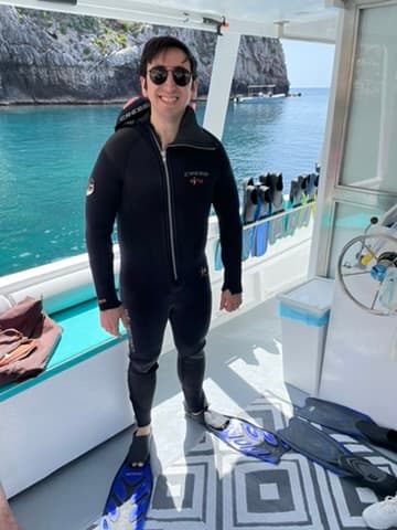 Matt in a wetsuit on a dive boat, fins on the deck beside him